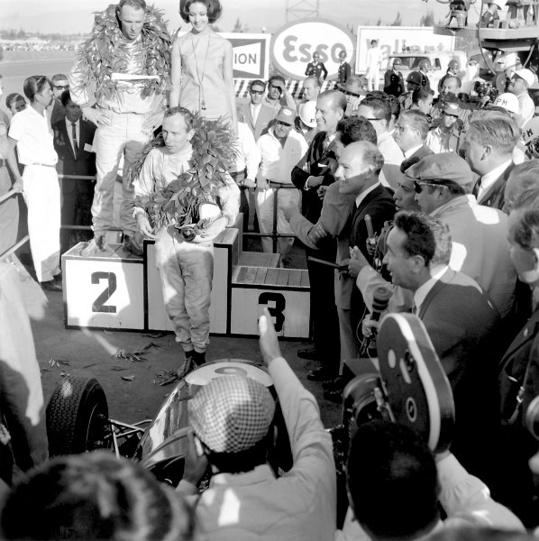 1964 Mexican Grand Prix.Mexico City, Mexico, 25 October 1964.John Surtees (Ferrari 158) celebrates on the podium as he becomes the only man to win World Championships on motorbikes and in a car. Racewinner Dan Gurney (Brabham BT7-Climax) looks on as does Stirling Moss. Ref-27505 40mb Scan from B&W PrintWorld Copyright: LAT Photographic 1964 Mexican Grand Prix.Mexico City, Mexico, 25 October 1964.John Surtees (Ferrari 158) celebrates on the podium as he becomes the only man to win World Championships on motorbikes and in a car. Racewinner Dan Gurney (Brabham BT7-Climax) looks on as does Stirling Moss. Ref-27505 40mb Scan from B&W PrintWorld Copyright: LAT Photographic